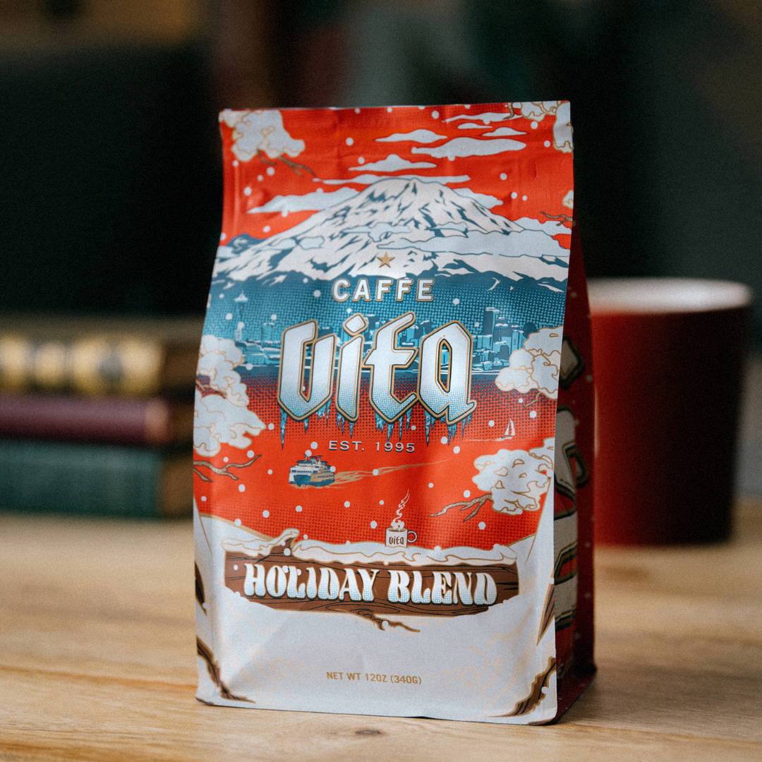 Image: 12oz Holiday Blend bag in front of books and mug.