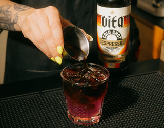 Hand pouring Vita Cold Shot into glass of ice and lemonade next to a bottle of Vita Cold Shot.
