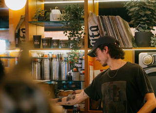 Caffe Vita's Capitol Hill cafe featuring a barista with various Vita branded cups, vinyls, and plants in the background.