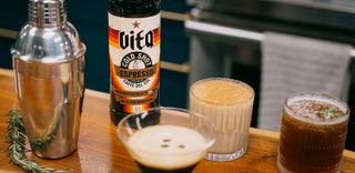 Vita Cold Shot on bar with various cocktails, cocktail shaker, and sprig of rosemary.