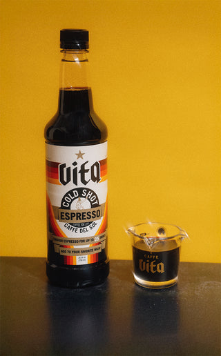 Bottle of Vita Cold Shot next to shot glass filed with Cold Shot with yellow background.