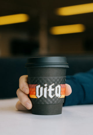 Hand holding Vita branded to go cup with sleeve and lid