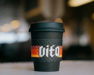 Vita branded to go cup with sleeve and lid on counter