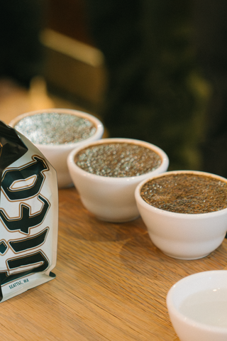 Coffee bag on a wooden table with small white cups containing coffee grounds.