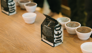 Coffee bag on a wooden table with small white cups containing coffee grounds