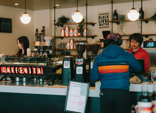 Caffe Vita's Seward Park cafe featuring a customer, two baristas, and a Caffe Vita branded espresso machine.