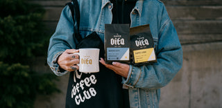 Person holding 12oz bags of Queen City and Caffe Luna along with a branded diner mug and tote.