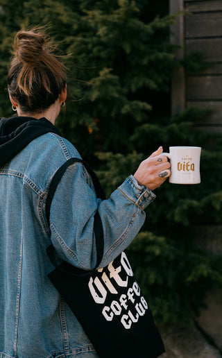 Person holding a branded diner mug and tote.