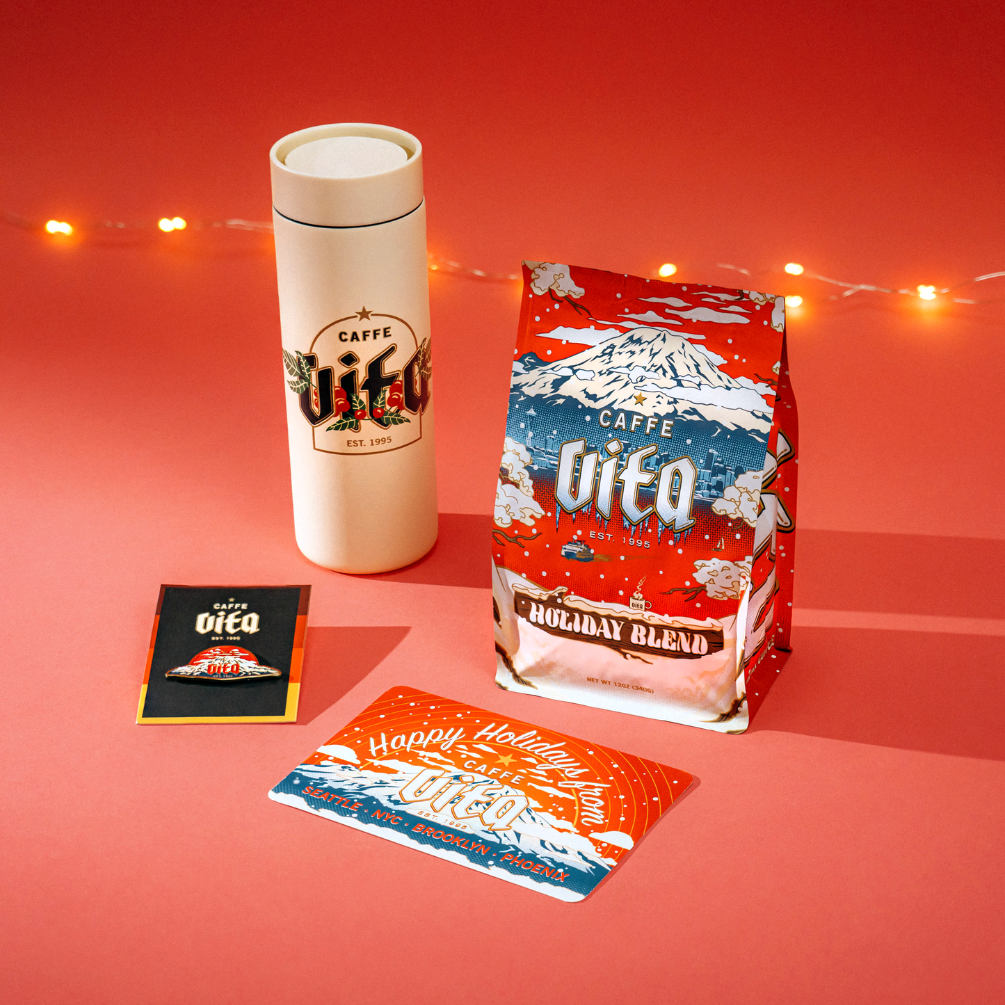 360 Traveler, mountain pin, holiday blend, and post card assembled on red background with tree lights.