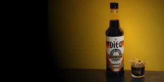 Bottle of Vita Cold Shot next to shot glass filed with Cold Shot with black and yellow gradient background.