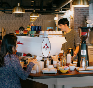 Barista making drinks behind espresso machine at a Vita wholesale customer cafe with customer in front of counter