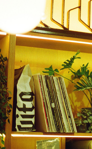 Bookshelves containing a 5lb bag of Vita coffee, various vinyls and plants with moody lighting.
