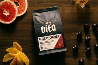 12oz bag of Cherry Cherry front, on wood slab with cut grapefruit, dried mangoes, cherries, and a Vita shot glass
