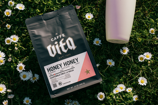 12oz bag of Honey Honey front, in grass and wildflowers next to white tumbler
