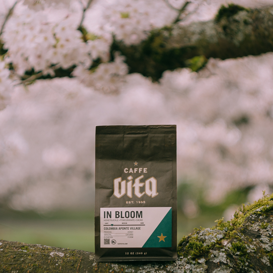Center foreground, 12oz bag of In Bloom balanced on a branch with cherry blossoms in the background. 