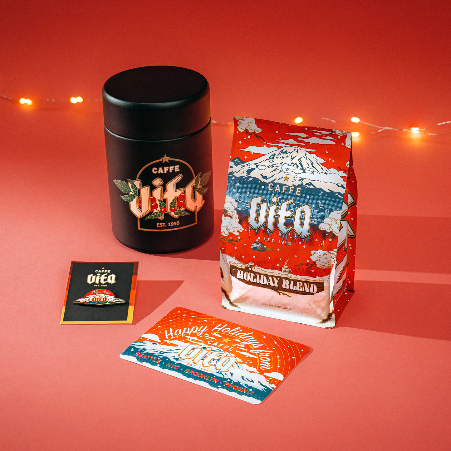 Coffee canister, mountain pin, post card, and holiday blend assembled on red background with tree lights.