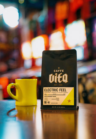 Caffe Vita coffee package with a yellow mug on a reflective surface, blurred background