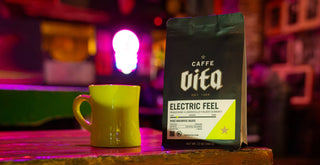 Caffe Vita coffee bag with a green mug on a wooden surface with a colorful background