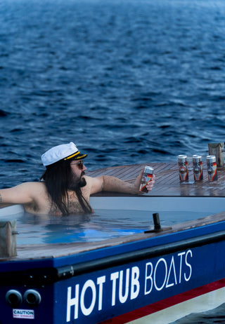 Person in a hot tub boat with 'HOT TUB BOATS' branding, holding a can of Vita cold brew.