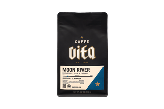 A 12 oz black coffee bag of Caffe Vita Moon River, featuring a cream and white label with a blue accent triangle, 
