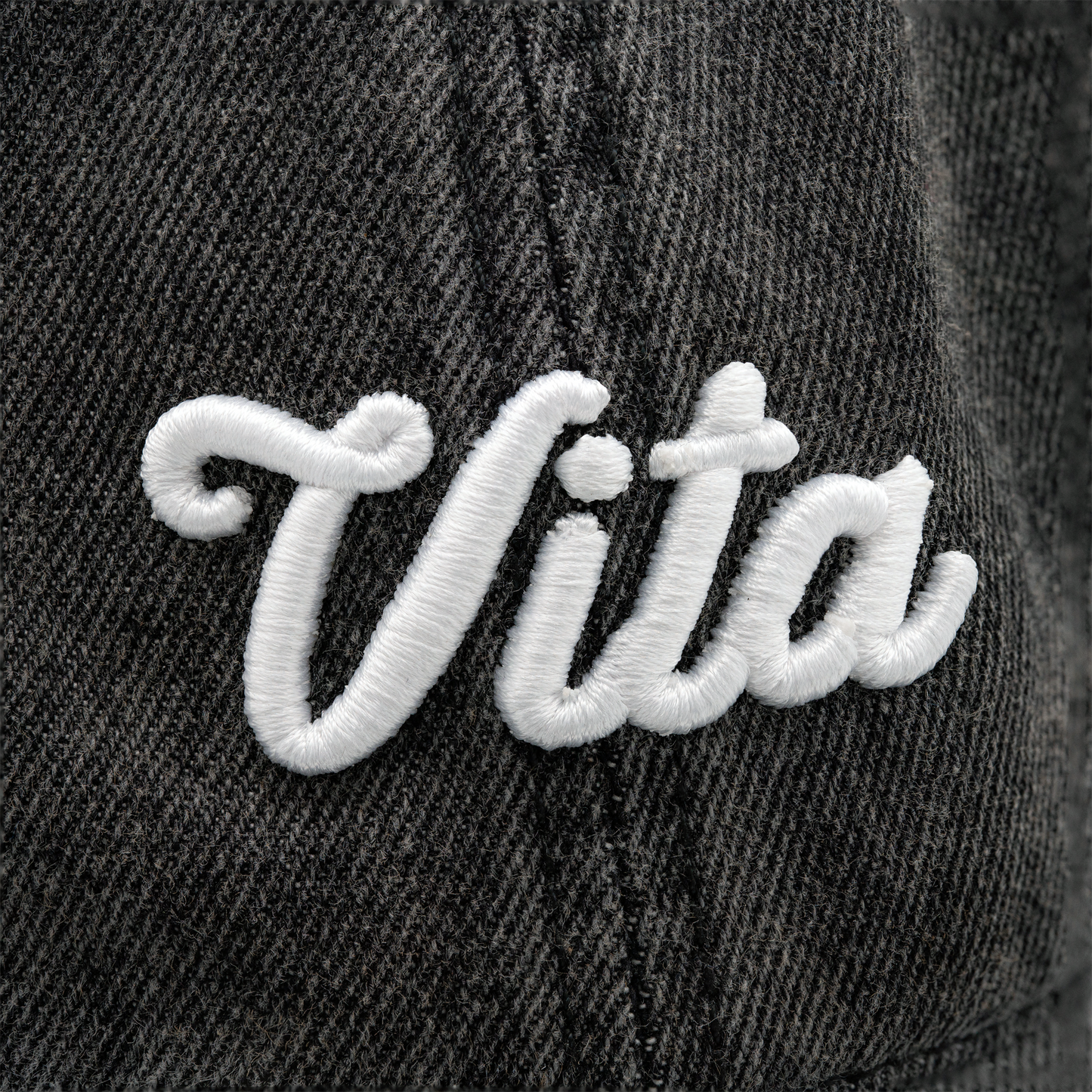Close up: white cursive Vita logo on front of baseball cap.